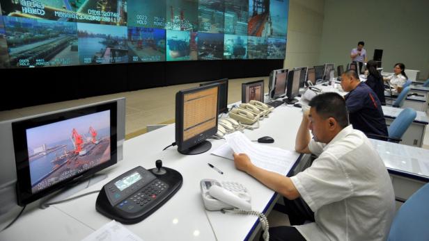 In einem Kontrollraum überwachen Mitarbeiter Monitore mit Hafenansichten.