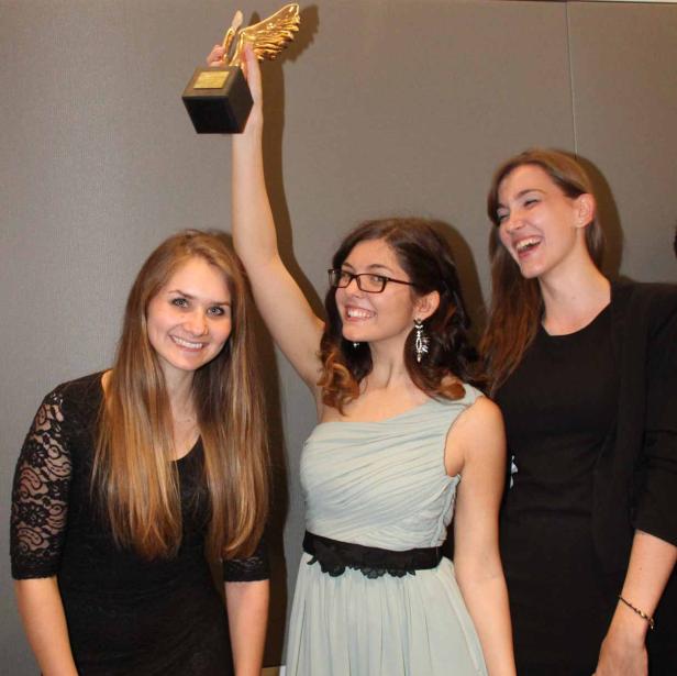Drei junge Frauen, eine davon hält einen goldenen Preis in die Höhe.