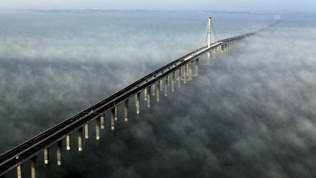Eine lange Brücke mit einem Pylon erstreckt sich über das Meer im Nebel.
