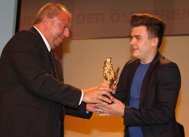 Ein Mann überreicht einem jungen Mann eine goldene Trophäe.