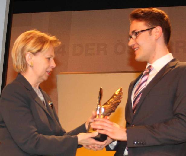 Eine Frau überreicht einem jungen Mann eine goldene Adler-Skulptur.