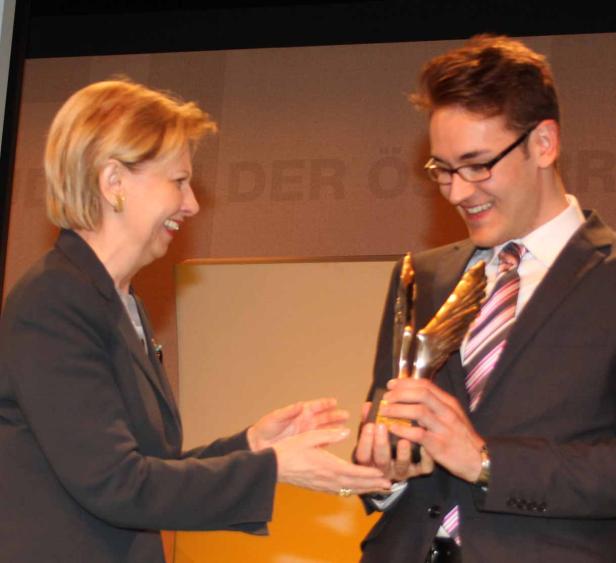 Eine Frau überreicht einem jungen Mann eine goldene Auszeichnung.