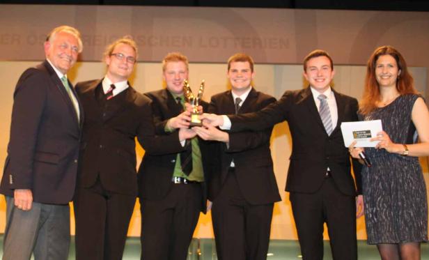 Eine Gruppe von Personen hält eine Trophäe auf einer Bühne.