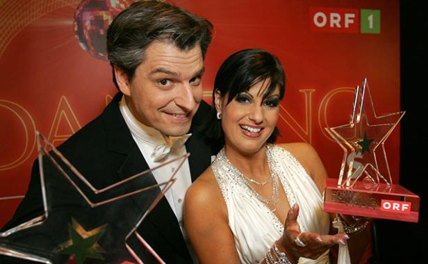 Ein Mann im Smoking und eine Frau im weißen Kleid halten Trophäen der ORF-Show „Dancing Stars“.