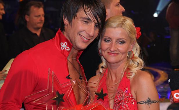 Ein Mann und eine Frau im roten Tanzoutfit halten Trophäen in Sternform.