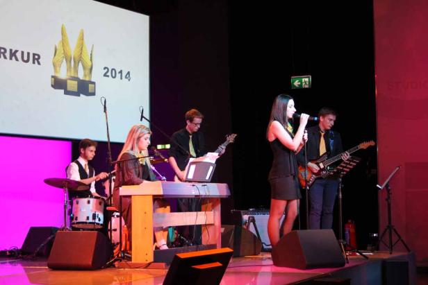 Eine Band tritt auf einer Bühne vor einer Leinwand mit der Aufschrift „2014“ auf.