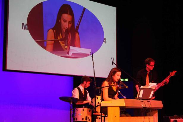 Eine Band tritt auf einer Bühne vor einer Leinwand auf.