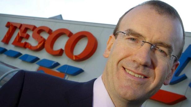 Ein Mann mit Brille lächelt vor einem Tesco-Supermarkt.
