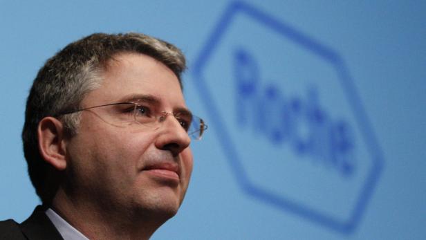 Ein Mann mit Brille vor einem blauen Hintergrund mit dem Roche-Logo.