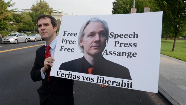 Ein Mann hält ein Schild mit einem Bild von Julian Assange und der Aufschrift „Free Speech Press Assange“.