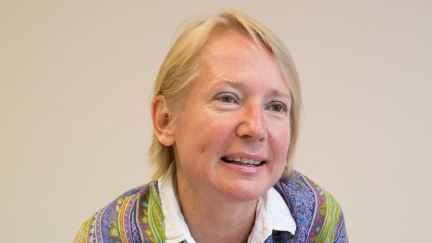 Eine Frau mit blonden Haaren und einem bunten Oberteil lächelt.