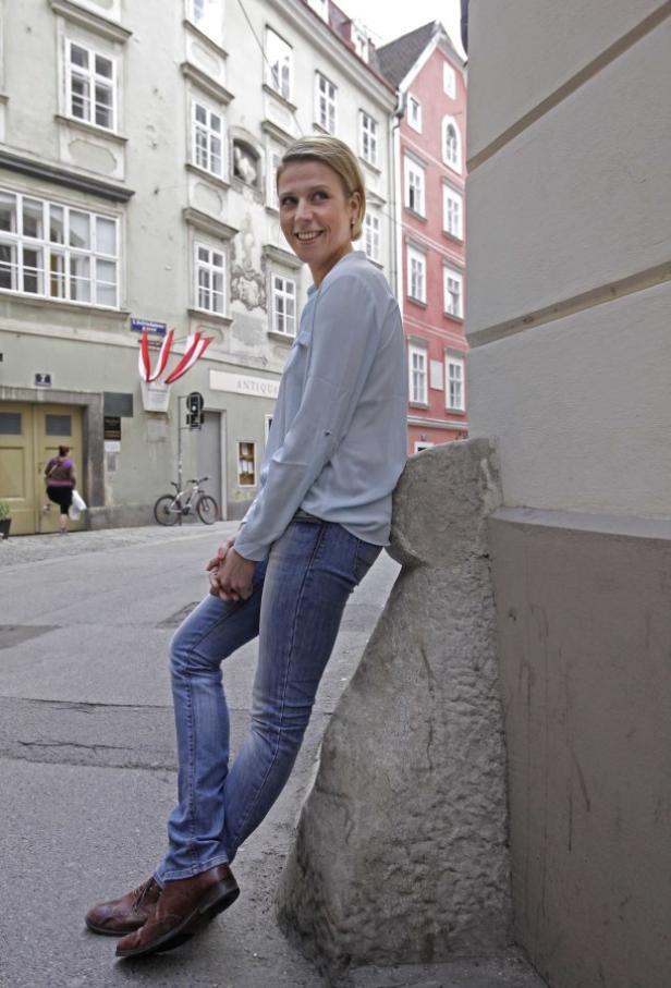 Eine Frau lehnt an einer Hausecke in einer Altstadt.
