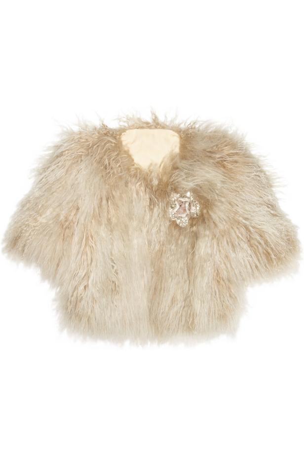 Eine kurze, beige Felljacke mit einer verzierten Brosche.