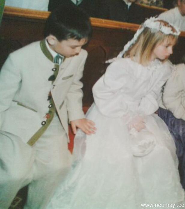 Ein Junge in Tracht und ein Mädchen im weißen Kleid sitzen nebeneinander.