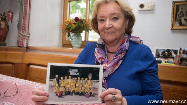 Eine Frau hält ein Foto einer Gruppe von Personen in gelber Schutzkleidung.