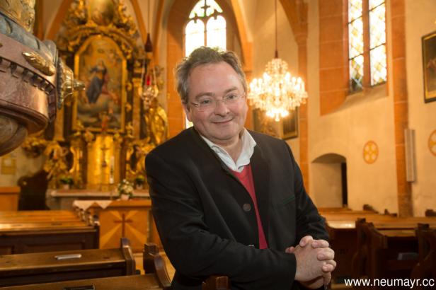 Ein Mann in Tracht steht in einer Kirche vor einem Altar.