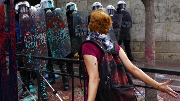 Eine Demonstrantin steht vor einer Reihe von Polizisten mit Schilden, die mit Farbe bespritzt sind.