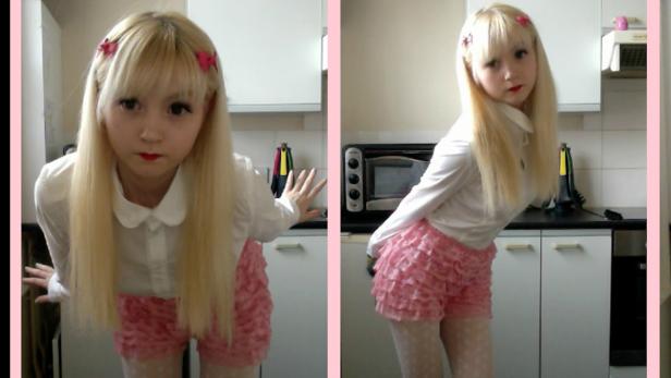 Eine junge Frau mit blonden Haaren und rosa Shorts posiert in einer Küche.