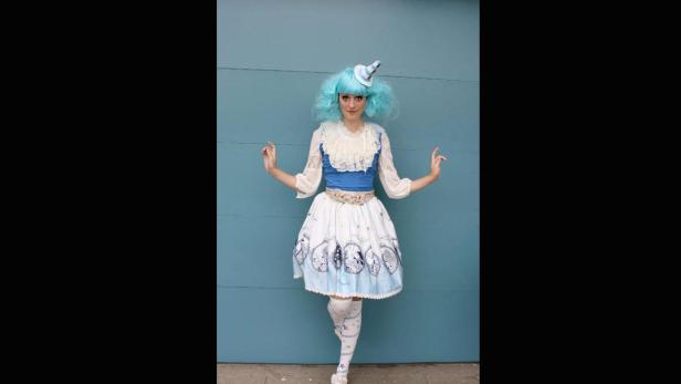 Eine Frau mit blauen Haaren und einem Partyhut posiert vor einer blauen Wand.