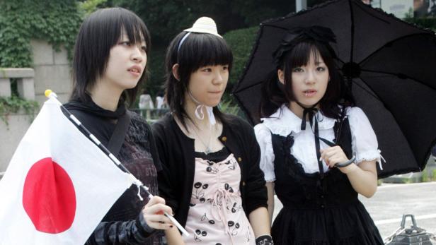 Drei junge Frauen im japanischen Stil, eine hält eine japanische Flagge, eine einen Sonnenschirm.