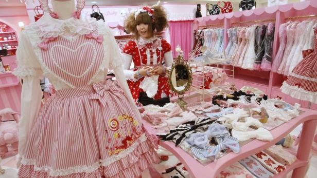Ein Mädchen in einem Lolita-Kleid steht in einem Geschäft mit rosa Kleidern und Accessoires.