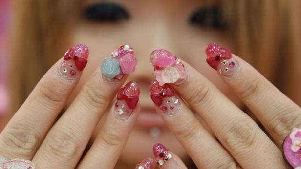Nahaufnahme von Händen mit aufwendig verzierten, rosafarbenen Nägeln.