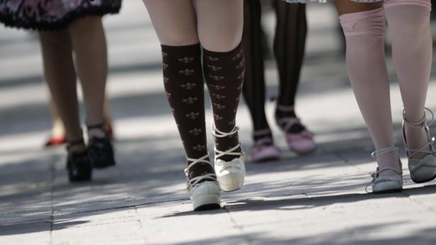 Mehrere Personen mit Strümpfen und Schuhen im Lolita-Stil stehen auf einem Gehweg.