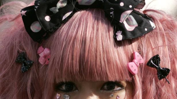 Nahaufnahme des Gesichts einer jungen Frau mit rosa Haaren und Schleifen im Haar.