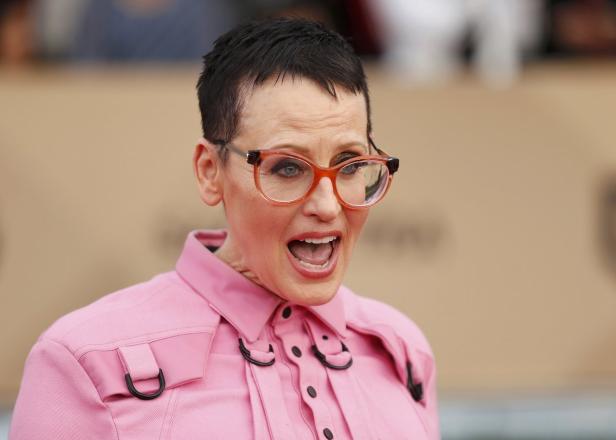 Eine Frau mit Brille und rosa Hemd schaut mit offenem Mund in die Kamera.