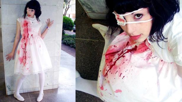 Eine junge Frau mit Augenklappe und blutverschmiertem Kleid posiert.