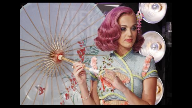 Katy Perry mit rosa Haaren, in einem hellblauen Kleid mit Blumen, hält einen verzierten Sonnenschirm.