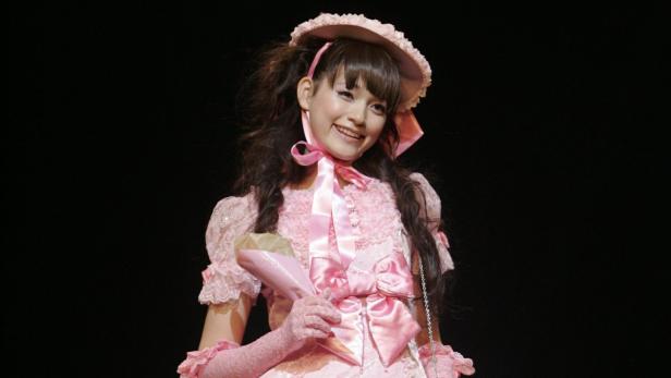 Ein junges Mädchen lächelt in einem rosa Kleid und Hut mit Schleifen.