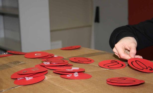 Eine Hand ordnet rote, runde Aufkleber mit einem schwarzen Symbol auf einem Karton an.