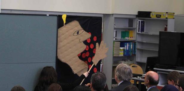 Eine Person führt ein Schattenspiel mit einer Pappfigur auf.