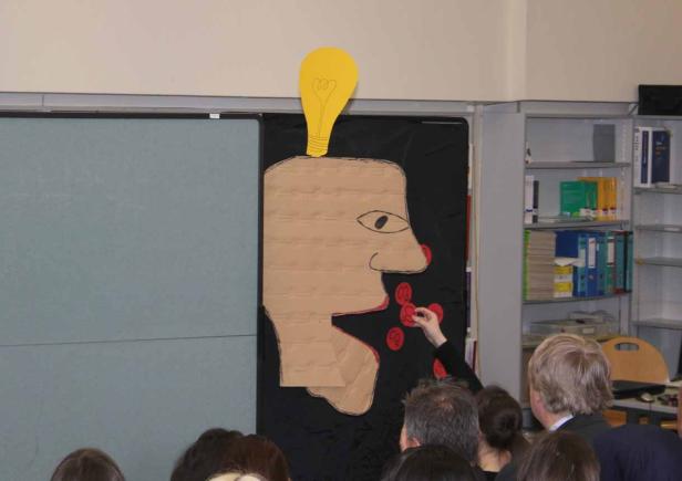 Eine Pappfigur mit einer Glühbirne auf dem Kopf wird mit roten Kreisen beklebt.