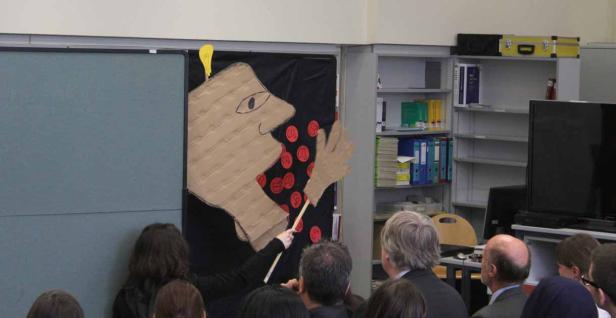 Eine Gruppe von Menschen betrachtet eine Pappfigur mit einer Glühbirne auf dem Kopf.