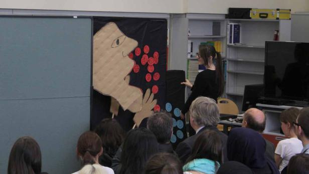 Eine Frau präsentiert ein Kunstprojekt vor einer Gruppe von Zuschauern.