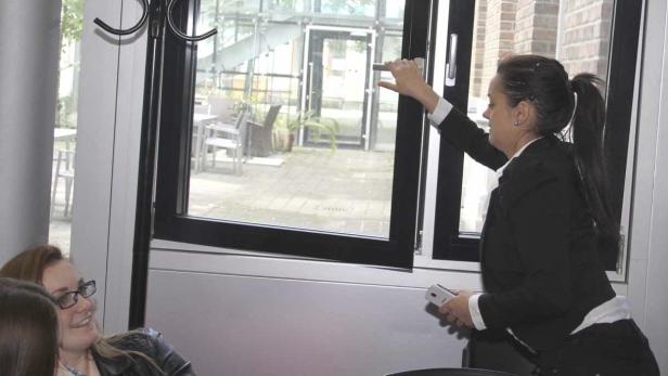 Eine Frau im Blazer öffnet ein Fenster, während zwei andere Frauen zusehen.