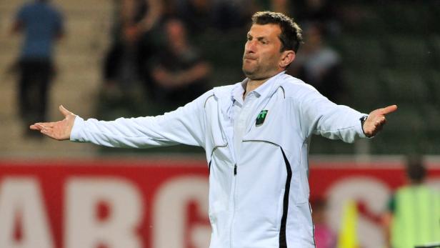 Ein Fußballtrainer gestikuliert mit ausgebreiteten Armen am Spielfeldrand.