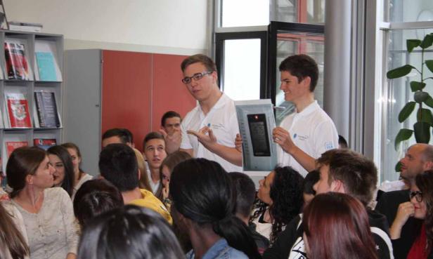 Zwei junge Männer präsentieren ein Gerät vor einer Gruppe von Zuhörern.