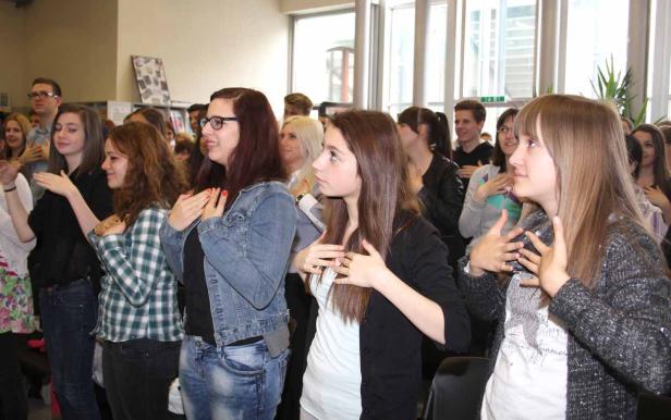 Eine Gruppe junger Leute steht und gestikuliert mit den Händen vor der Brust.