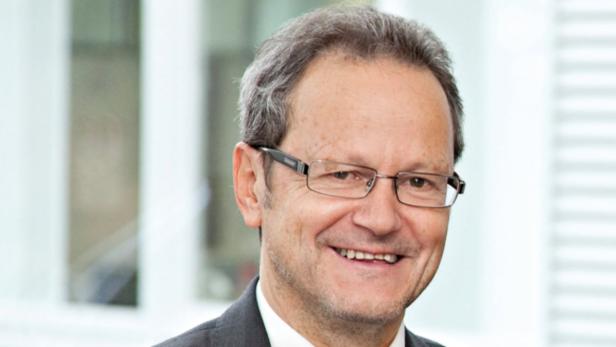 Ein lächelnder Mann mit Brille und grauem Haar in einem Anzug.
