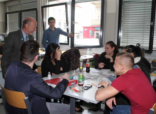 Eine Gruppe von Schülern sitzt mit einem Lehrer an einem Tisch in einem Klassenzimmer.