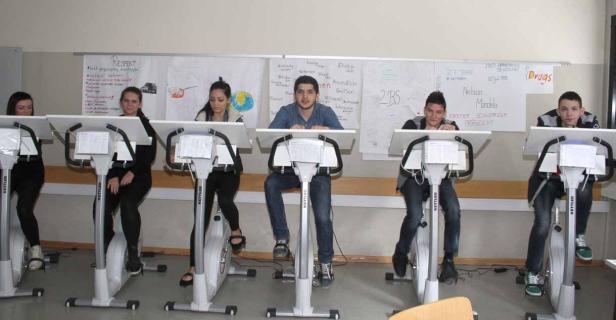 Eine Gruppe von Schülern sitzt auf stationären Fahrrädern in einem Klassenzimmer.