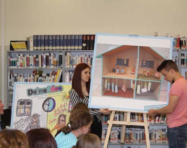 Schüler präsentieren Plakate und ein Modellhaus in einer Bibliothek.
