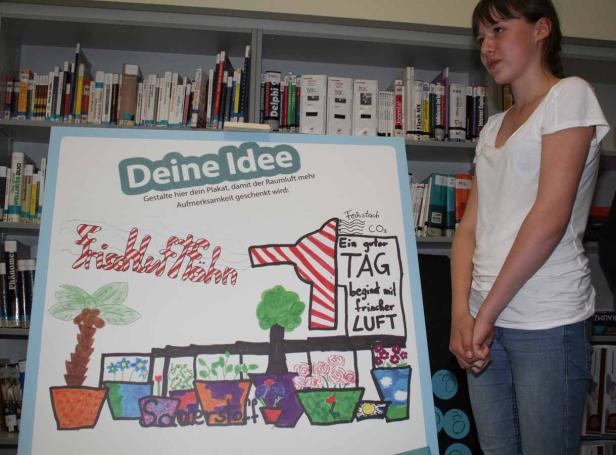 Ein junges Mädchen steht neben einem Plakat mit der Aufschrift „Deine Idee“ und Zeichnungen von Pflanzen.