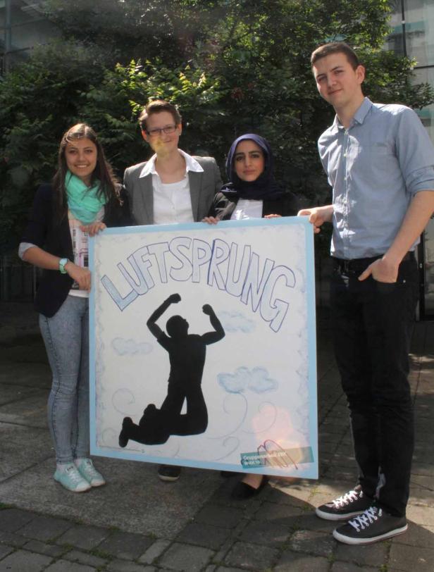 Vier junge Leute präsentieren ein Plakat mit der Aufschrift „Luftsprung“.