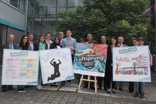 Eine Gruppe von Personen präsentiert Plakate zum Thema „Luftsprung“ für frische Luft in Klassenzimmern.