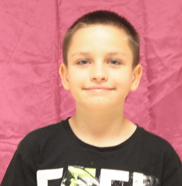 Ein lächelnder Junge mit kurzem Haar vor einem rosa Hintergrund.