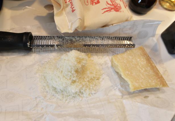 Ein Stück Parmesan liegt neben einer Reibe und geriebenem Käse.